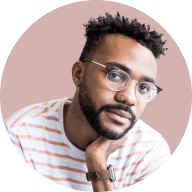 Man with glasses and short curly hair resting his chin on his hand against a light pink background.